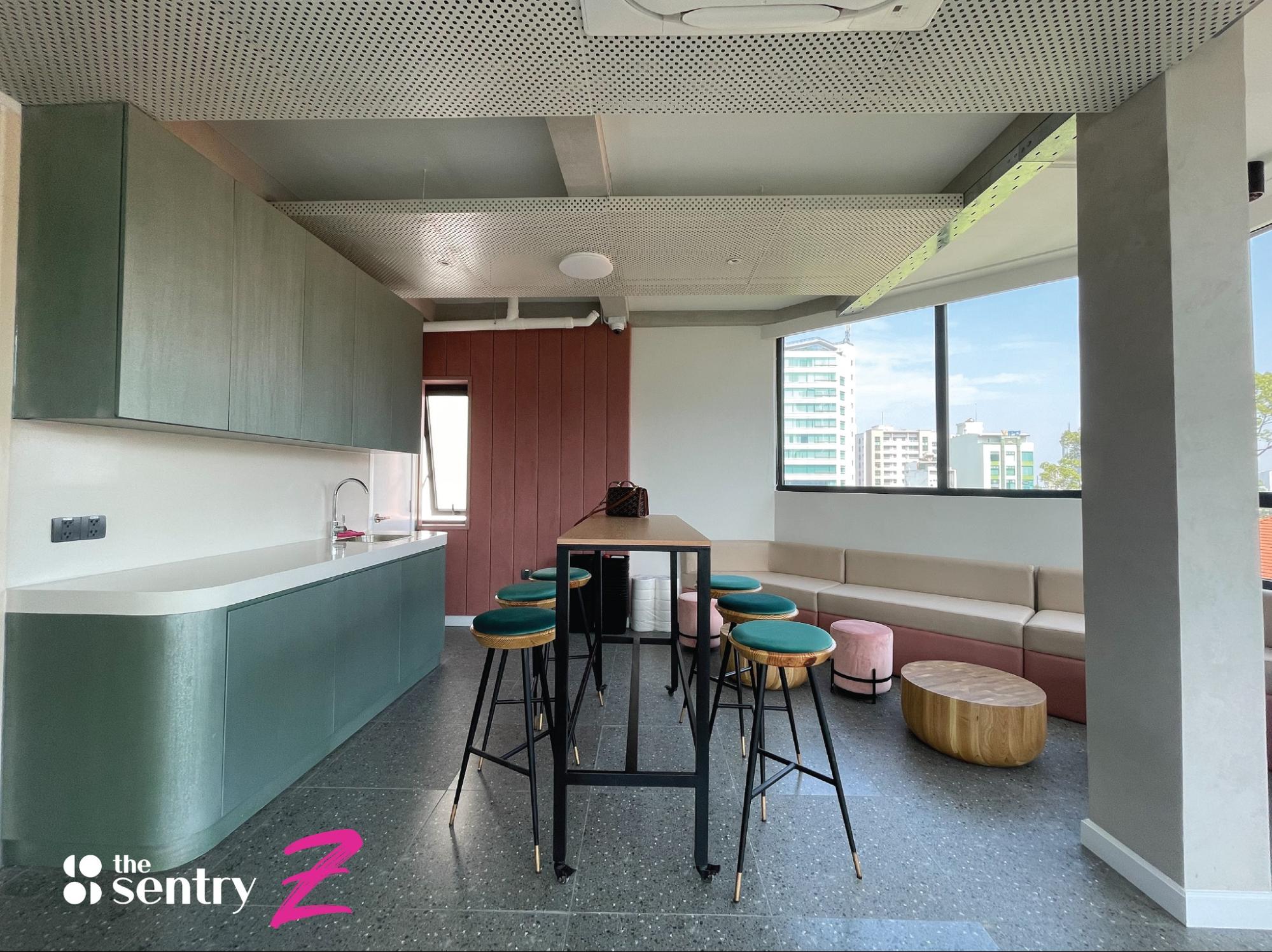 A kitchen area in a coworking space with green cabinets and high stools.