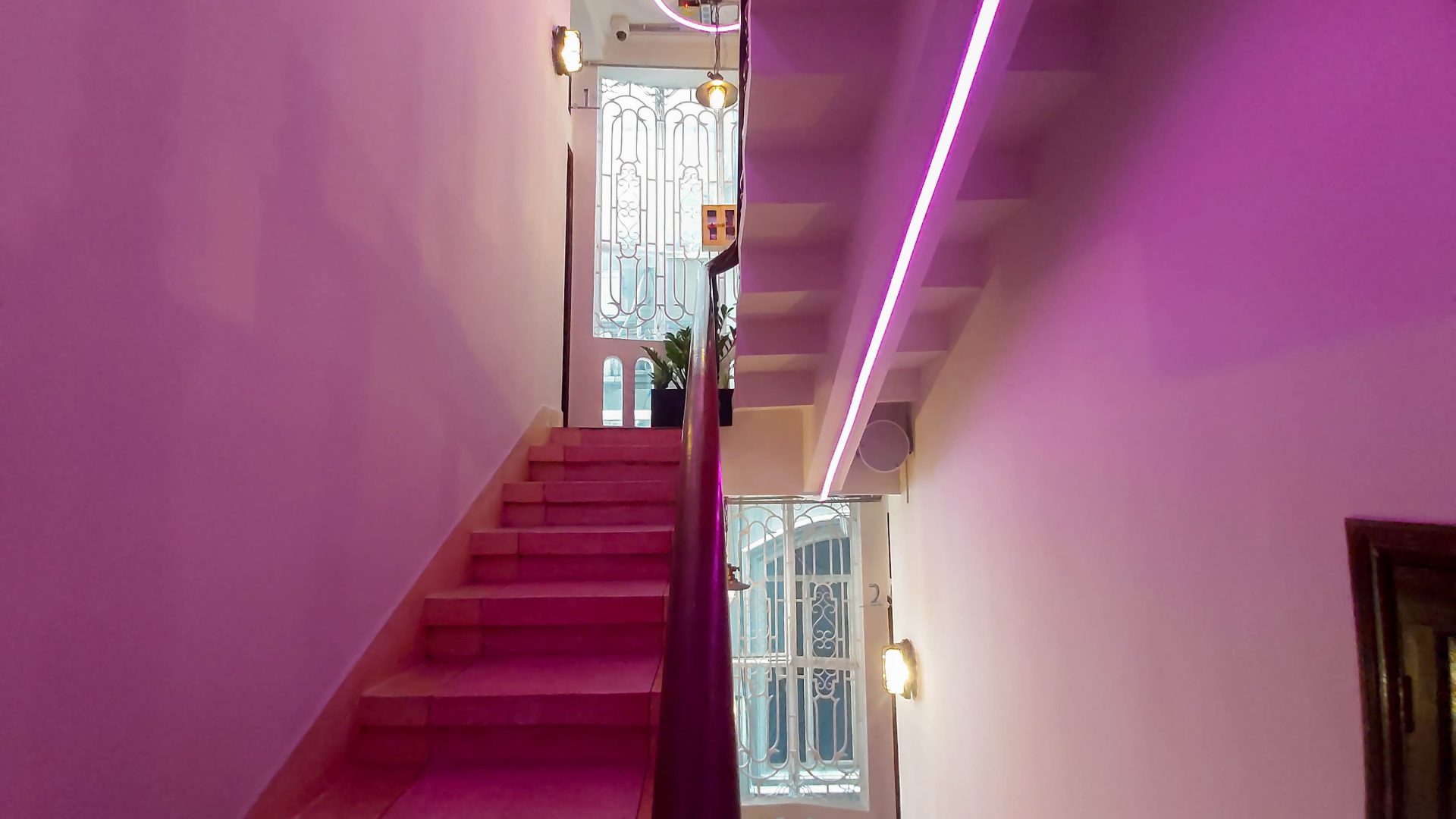 A staircase with a modern design, illuminated by purple lighting, leading to a door with intricate glasswork at The Sentry L