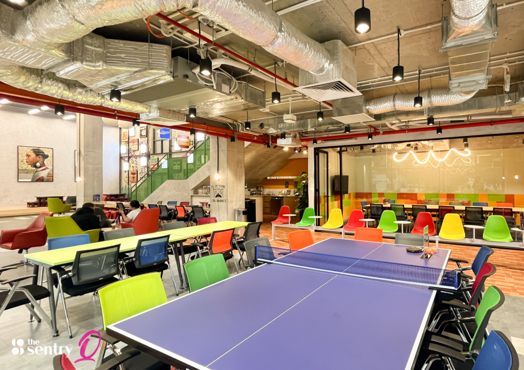 A spacious view of an open-plan coworking workspace featuring hot desks, private suites, and a central lounge.